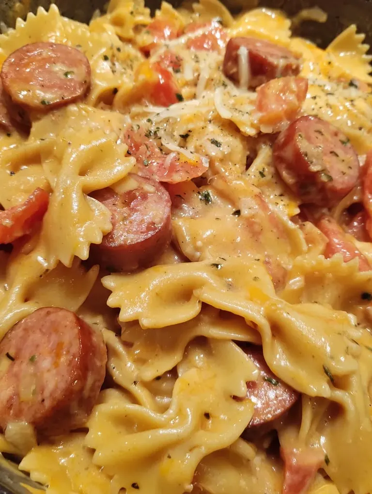 A bowl of pasta with sausage and tomatoes.