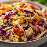 A bowl of salad with purple cabbage, corn, tomatoes, and lettuce.