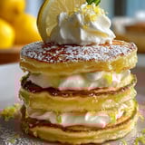 A stack of pancakes with lemon and whipped cream on top.