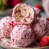 A plate of pink cake with red frosting and strawberries.