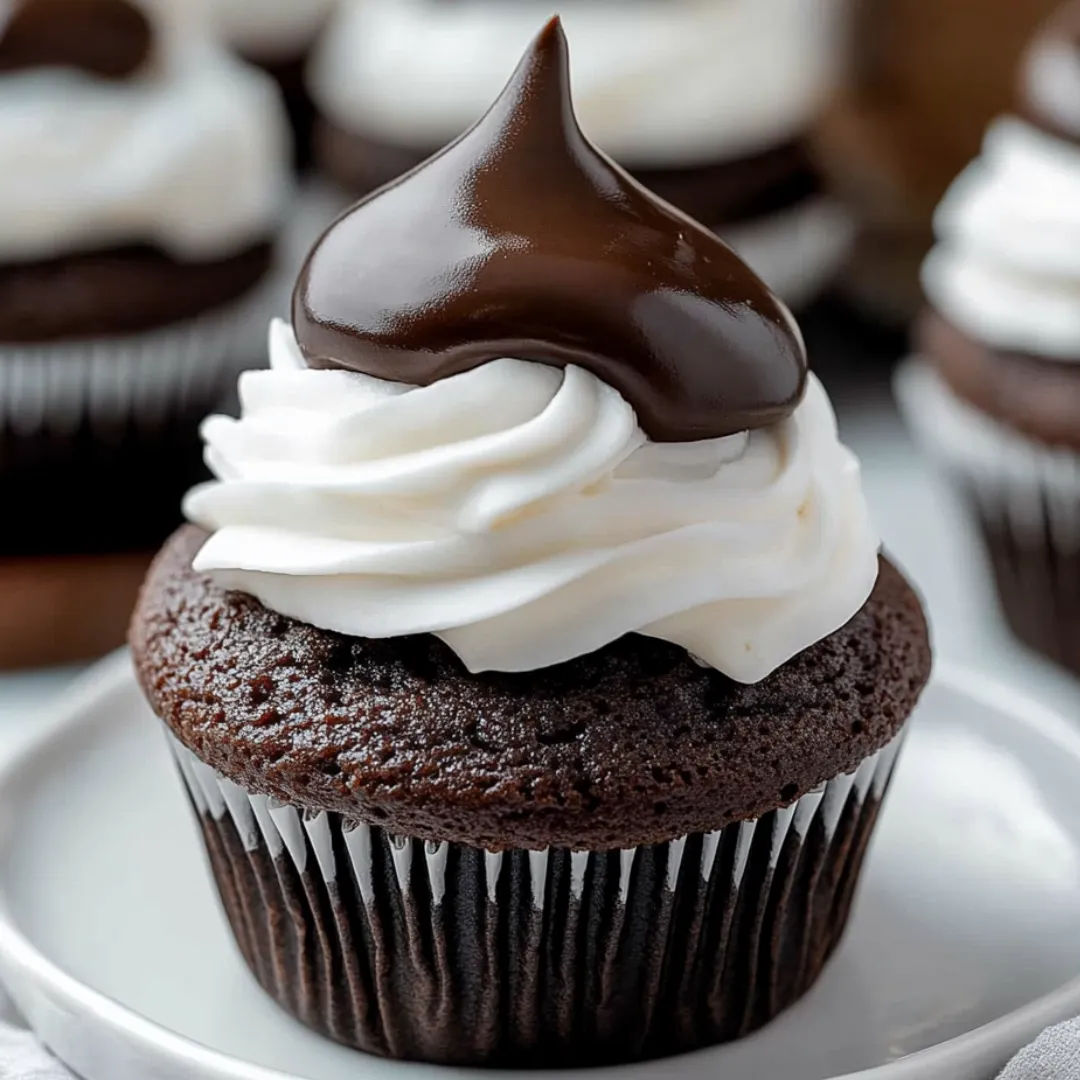 A cupcake with a chocolate frosting and white whipped cream on top.