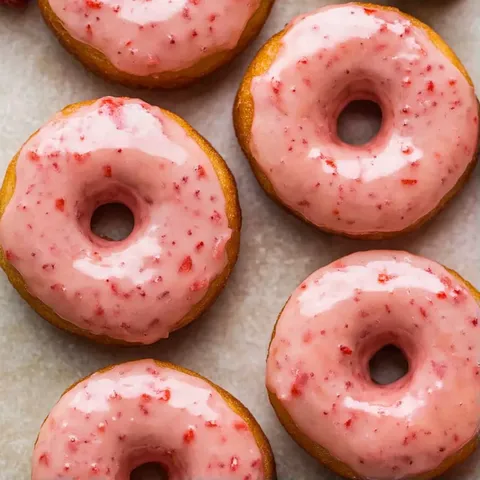 A table full of donuts with pink frosting and red sprinkles.