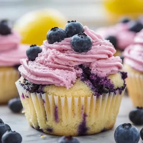 A cupcake with blueberries and pink frosting.
