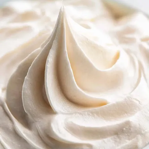 A white cream is in a bowl and it has a spoon in it.