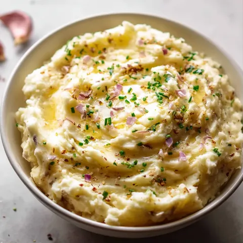 A bowl of mashed potatoes with green herbs.