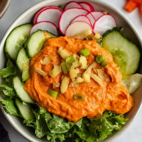 A bowl of salad with red sauce and sliced vegetables.