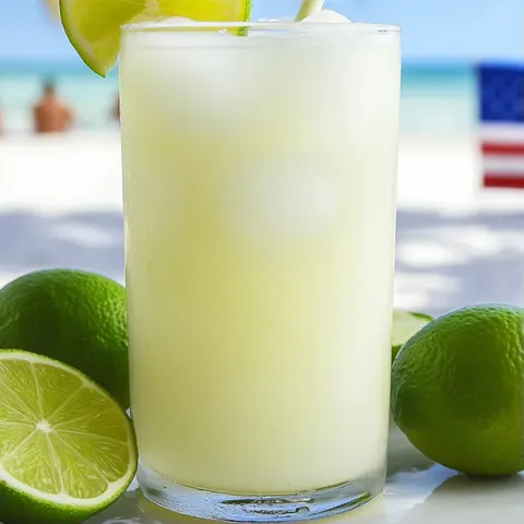 A glass of limeade with limes on the side.