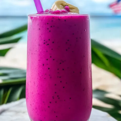 A glass of pink smoothie with a purple straw.