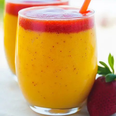 A glass of orange juice with a strawberry on the side.