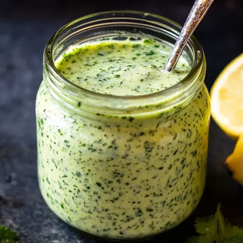 A jar of green sauce with a spoon in it.