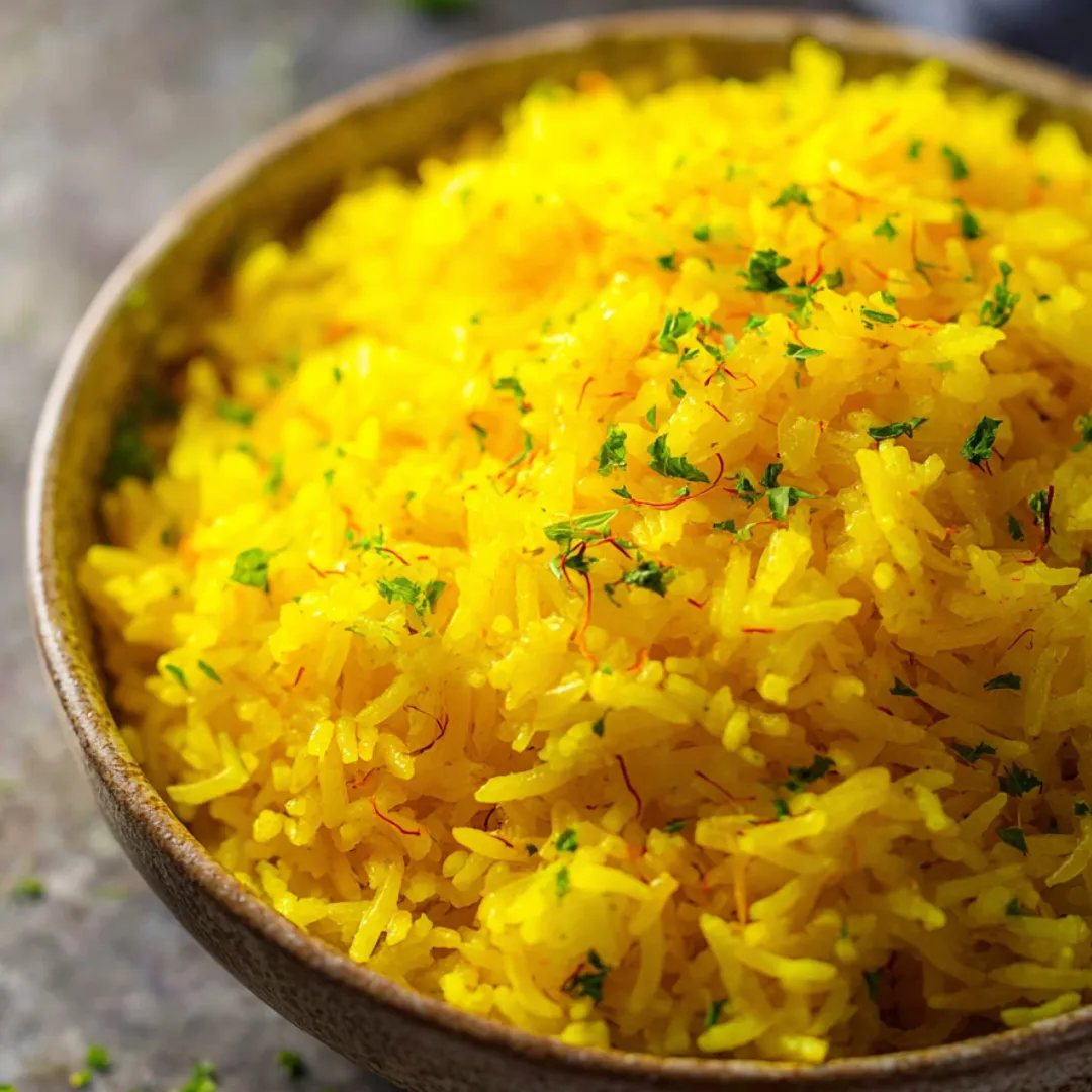 A bowl of yellow rice with green herbs on top.