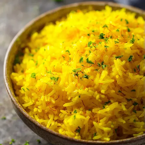 A bowl of yellow rice with green herbs on top.