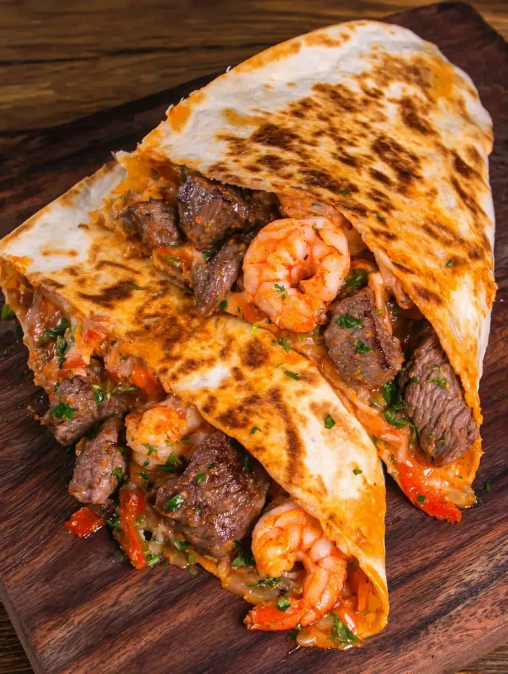 A burrito with shrimp and meat on a wooden table.