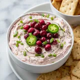 A bowl of dip with green onions and red cherries.