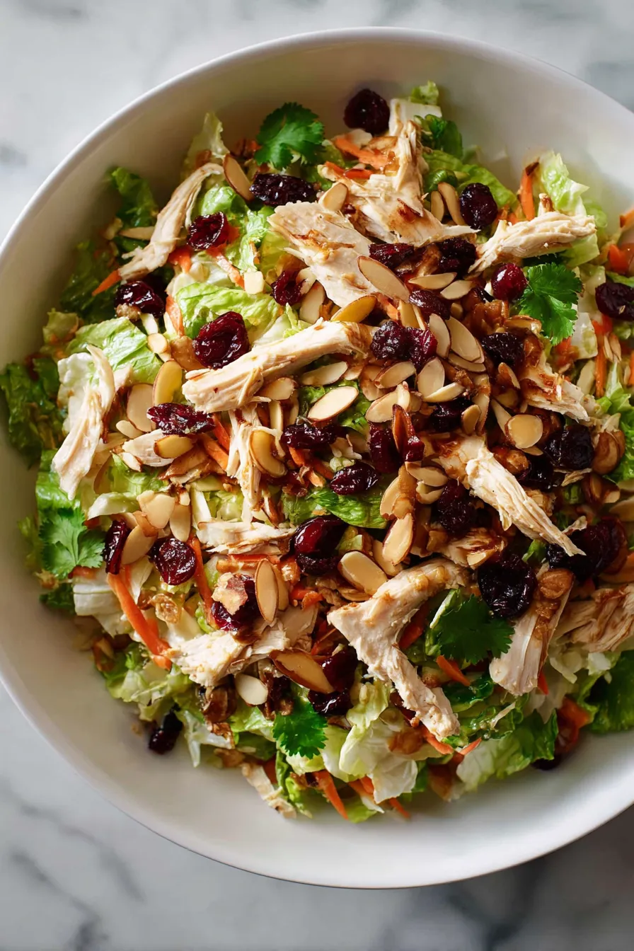 A bowl of salad with chicken, cranberries, and almonds.