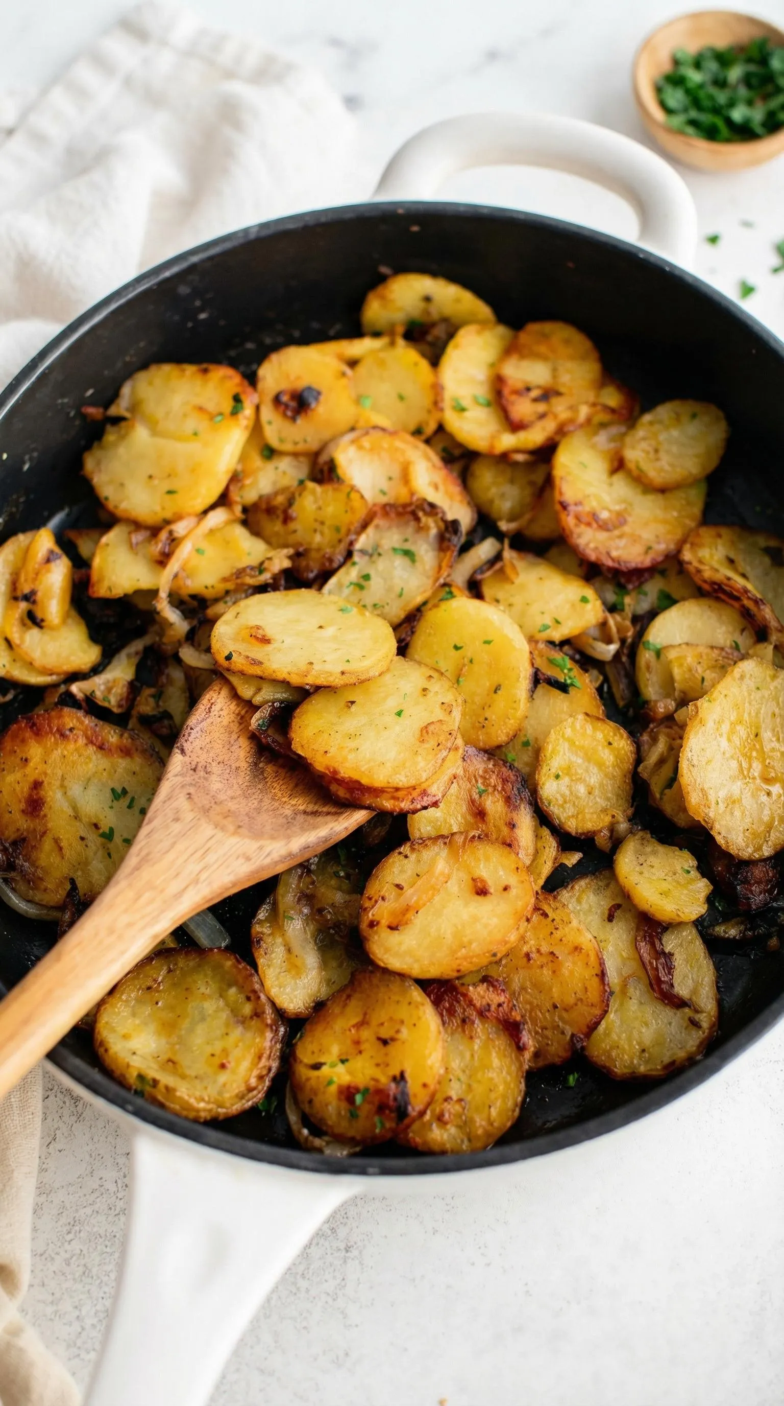 A pan of potatoes with a wooden spoon.