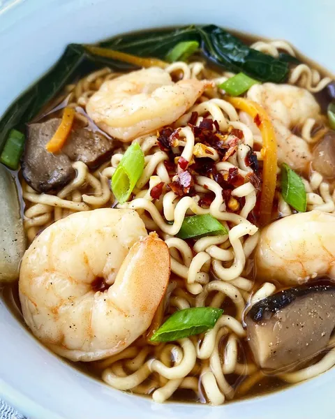 A bowl of noodles with shrimp, vegetables, and spices.