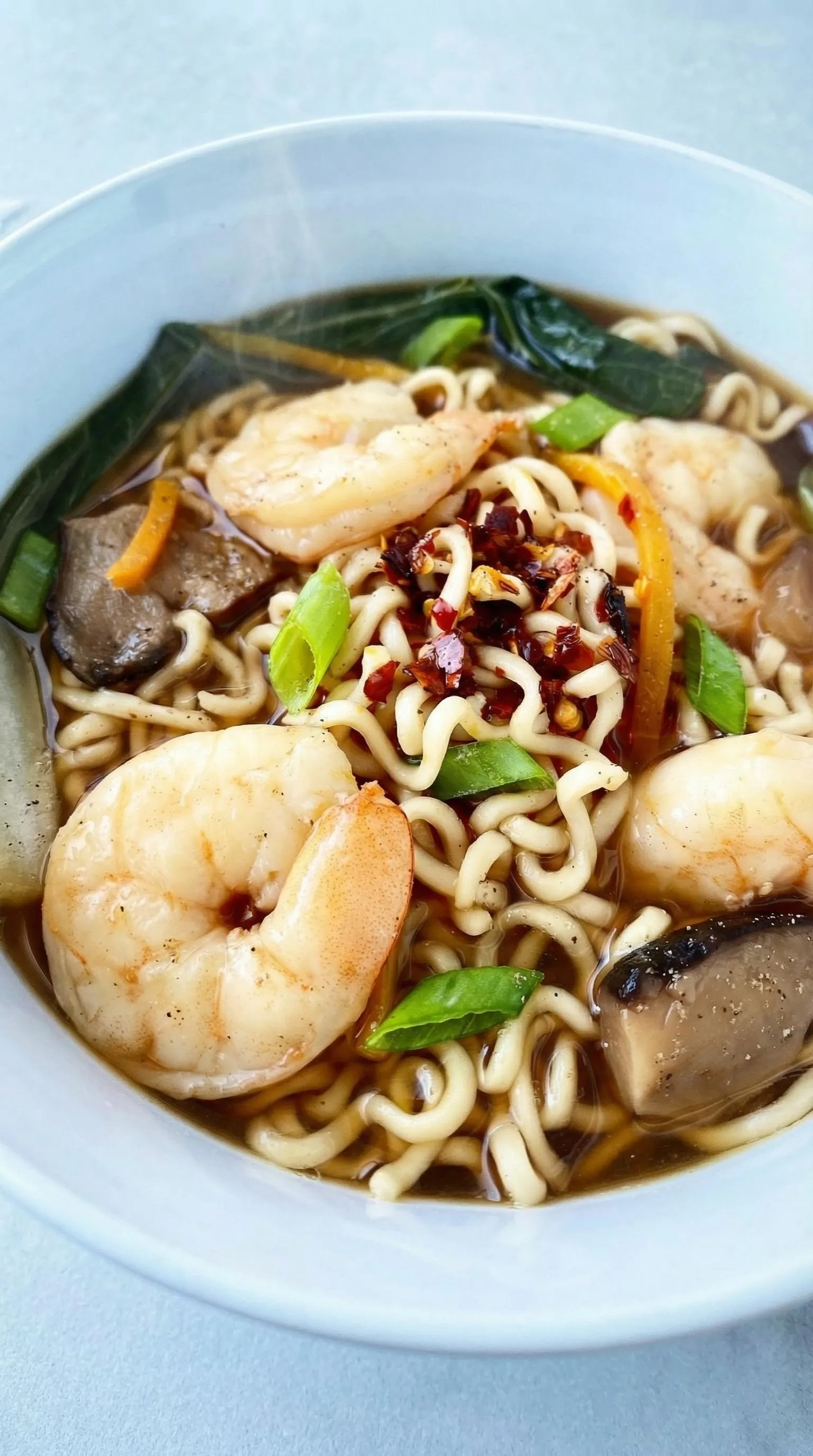 A bowl of noodles with shrimp and vegetables.