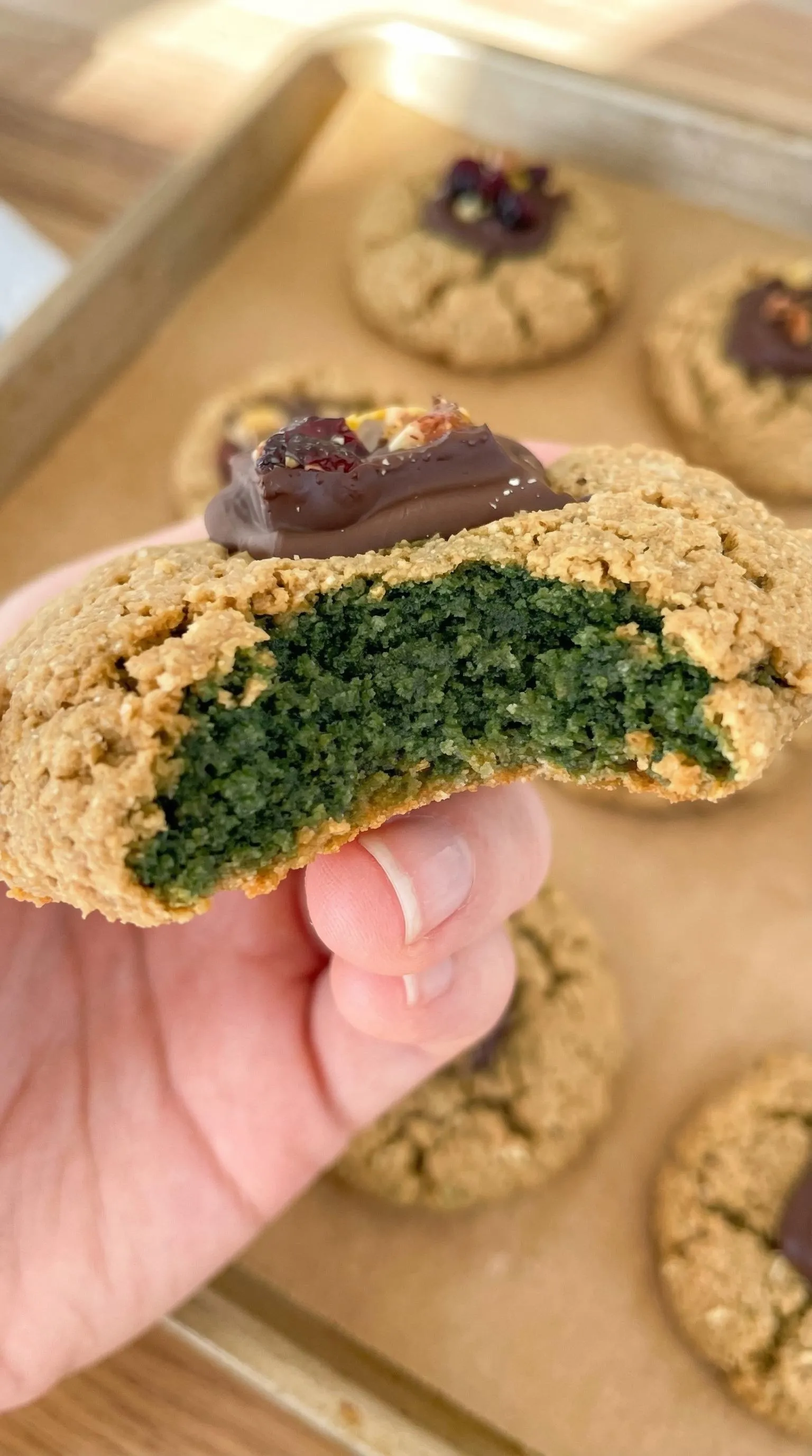 A person holding a cookie with chocolate and green icing.