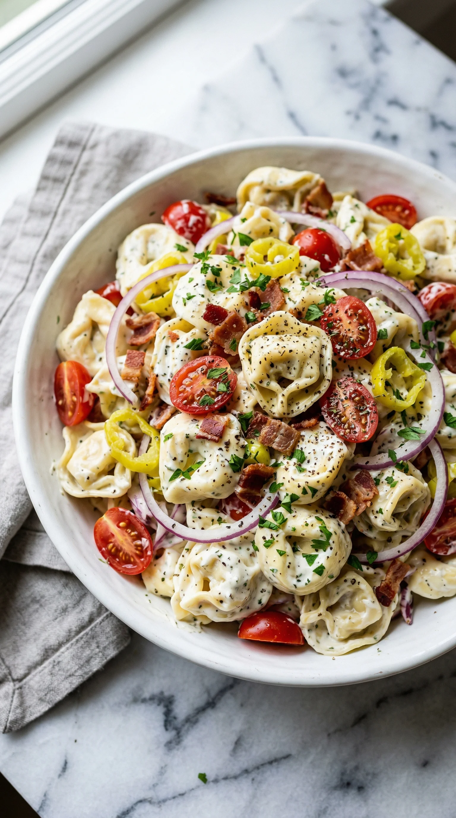 A bowl of pasta salad with tomatoes, onions, and bacon.
