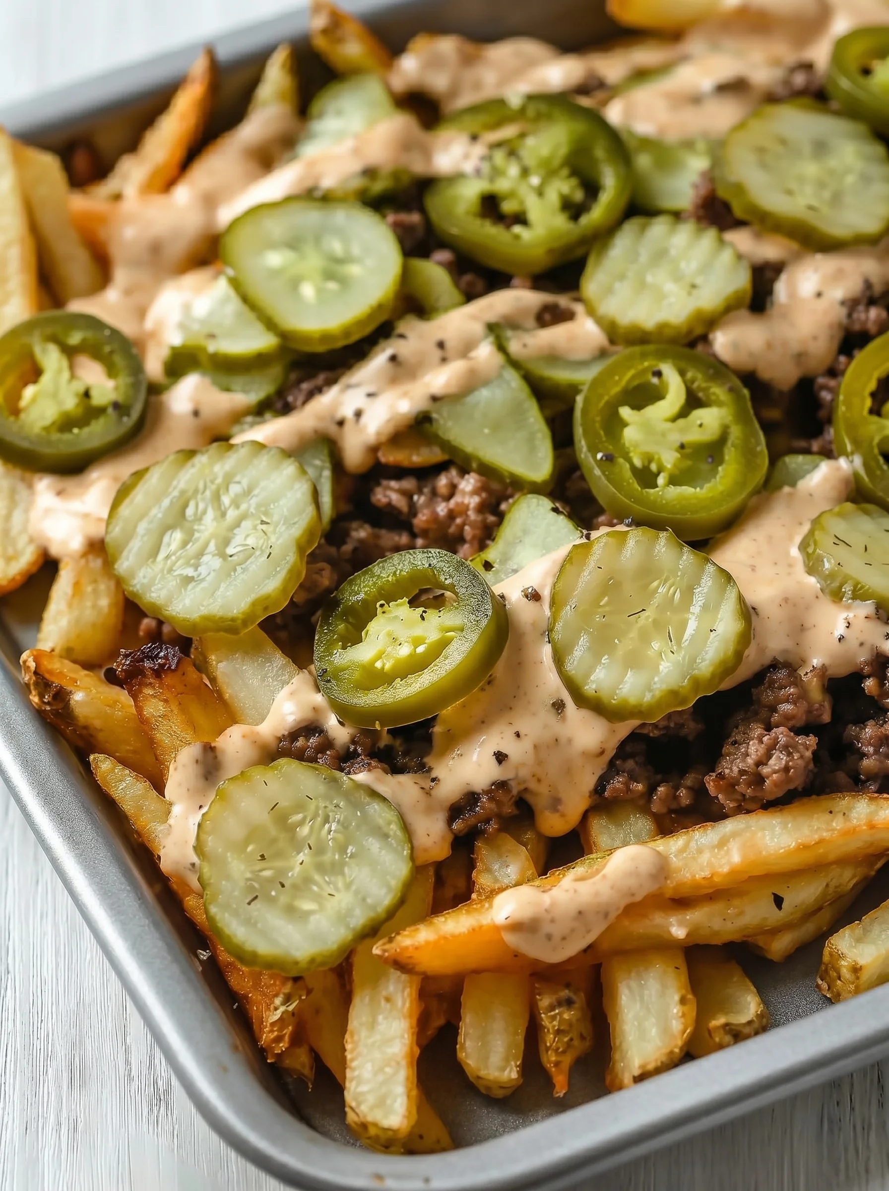 A plate of smash burger fries with jalapenos and cheese.