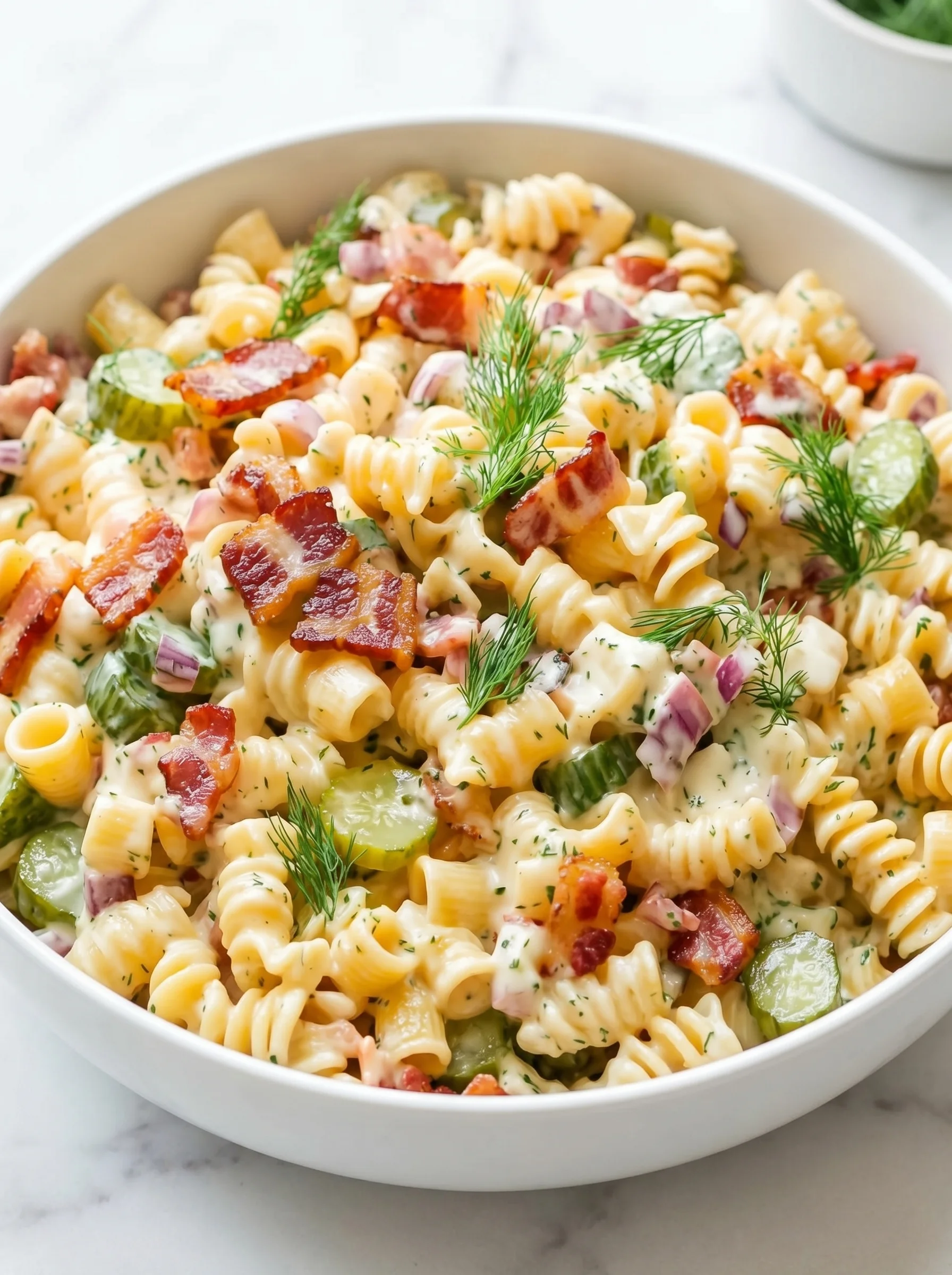 A bowl of pasta salad with bacon and dill pickles.