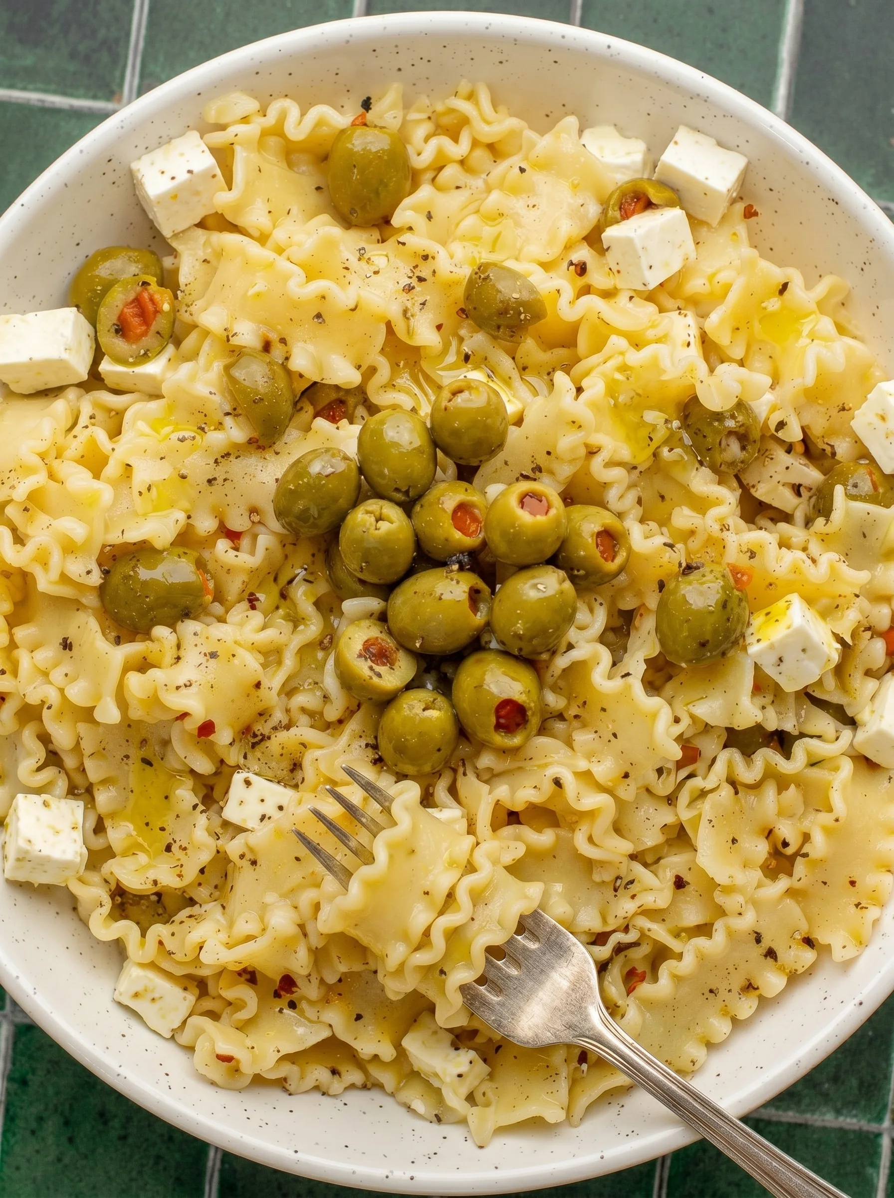 A bowl of pasta salad with olives and cheese.