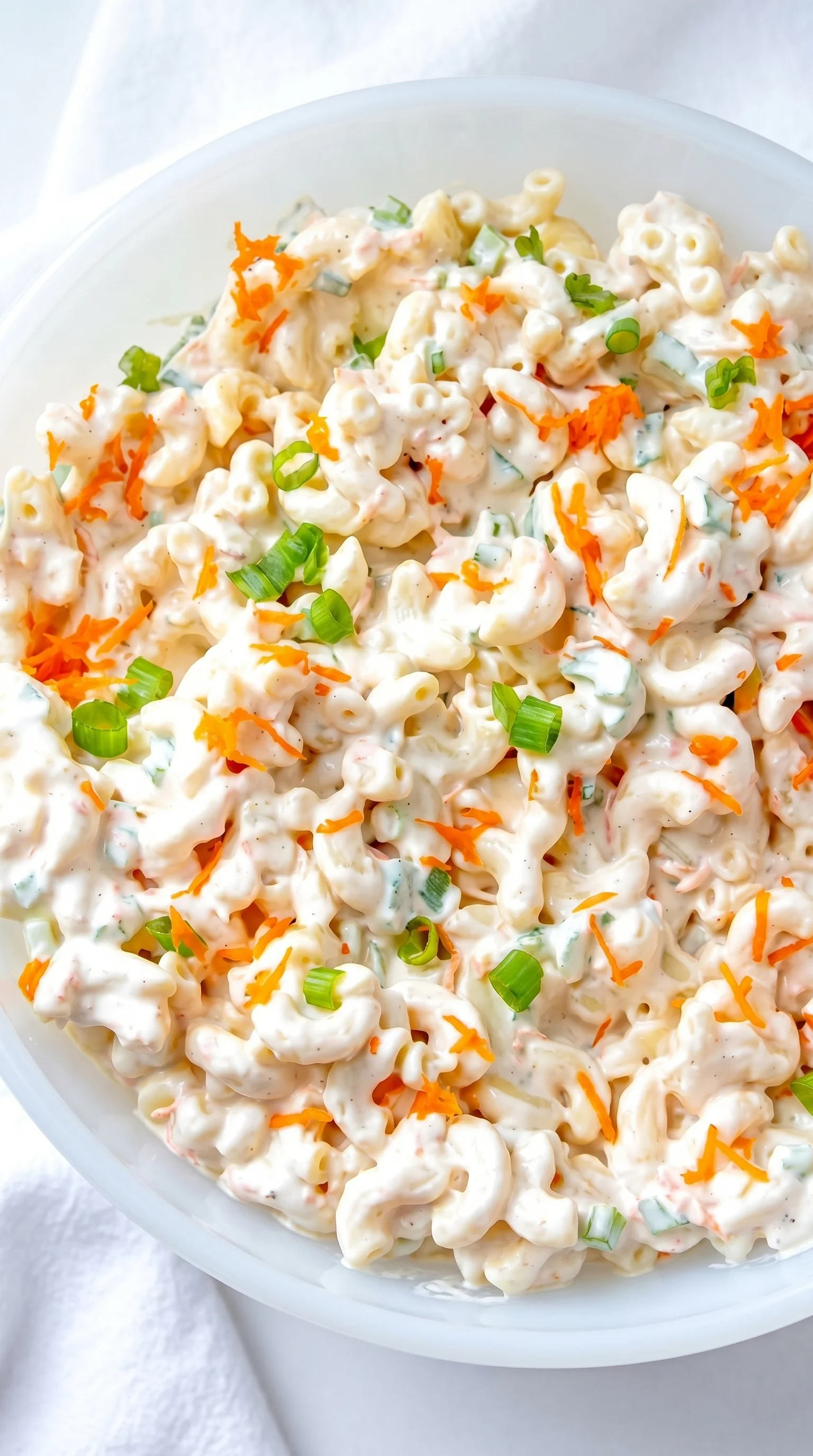 A bowl of macaroni salad with carrots.