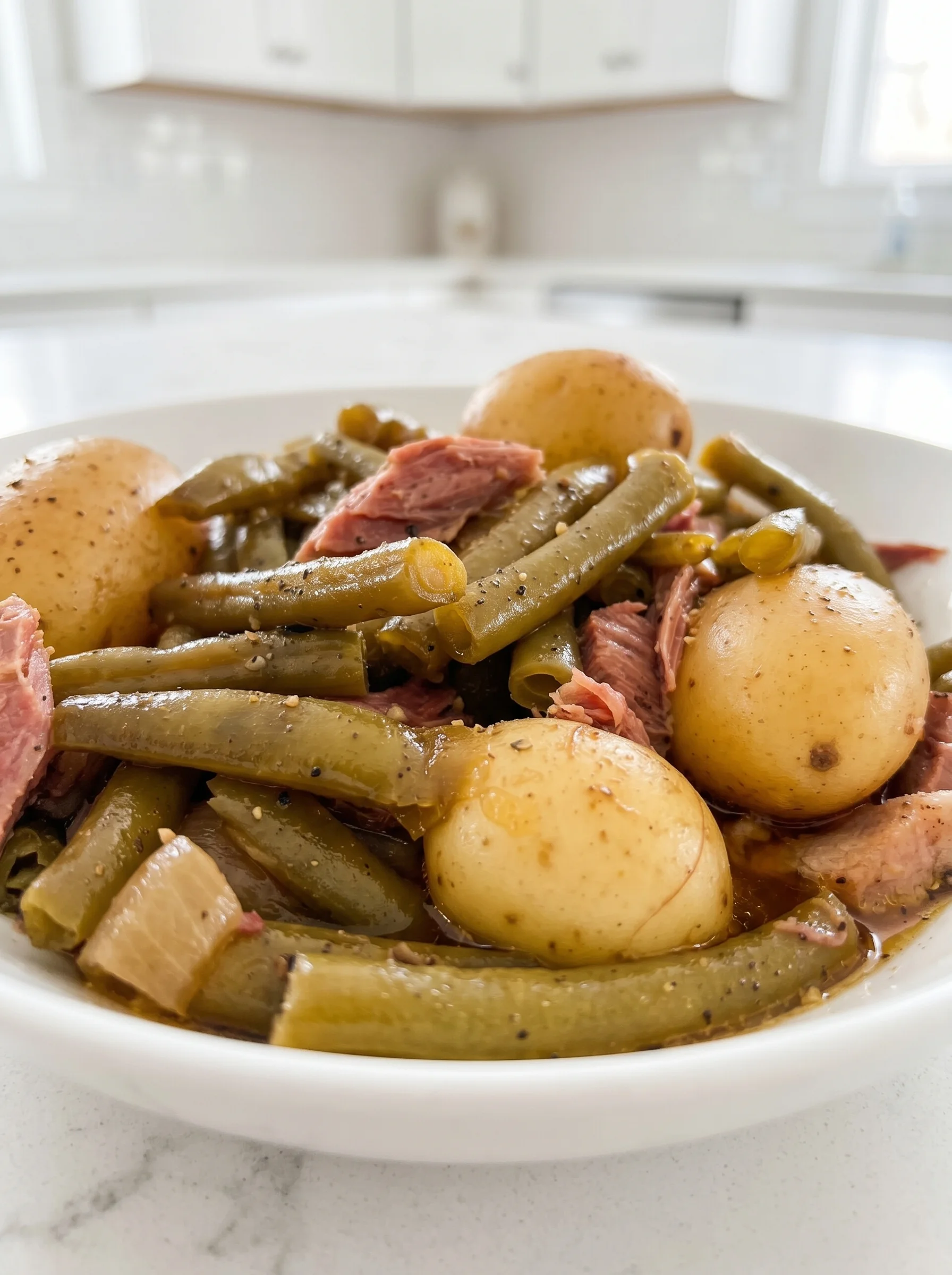 A white plate with a bowl of slow cooker green beans, ham and potatoes.