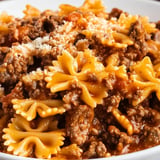 A bowl of spaghetti with meat sauce and cheese on top.