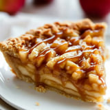 A slice of pie with caramel sauce on a white plate.