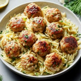 A plate of pasta with meatballs and a lemon wedge on the side.