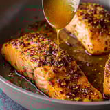 A pan of fish with a spoon of honey drizzled over it.