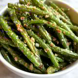 A bowl of green beans with seasoning.